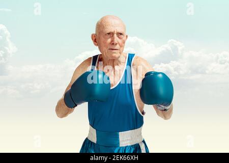 Senior man wearing sportwear boxing isolated on sky background. Caucasian male model in great shape stays active and sportive. Concept of sport, activity, movement, wellbeing. Copyspace, ad. Stock Photo