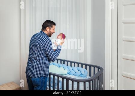 Proud father holding newborn baby daughter next to crib Stock Photo