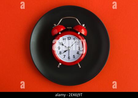 Red alarm clock on the black plate on the red background.  Top view. Stock Photo