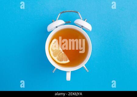 Top view of tea on the dial of the white alarm clock in the center of the blue background Stock Photo