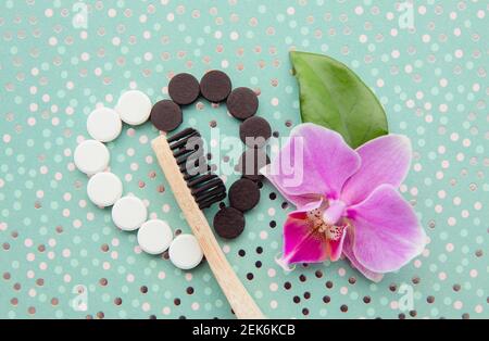 Top view of black activated charcoal and white fluoride toothpaste tablets. Dental care concept. Minimal mint green dotted background with pink orchid Stock Photo