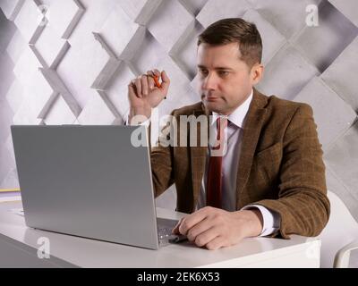 Manager with pen and papers reads data on a laptop screen. Stock Photo
