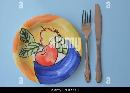 Empty ceramic side plate with a fruit design, and knife and fork Stock Photo