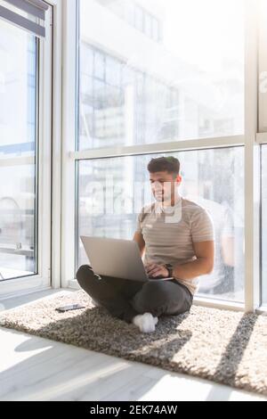 Young man working on laptop sitting on floor. Guy with computer reading news, surfing net or freelancing Stock Photo