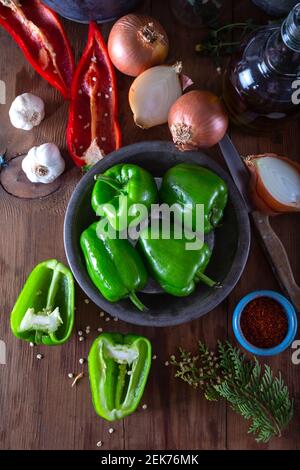 Food preparation with fresh green bell pepper. Fresh green bell pepper and red pepper with onion, garlic and spices on natural wooden background. Stock Photo