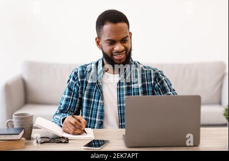 Cheerful African Businessman Taking Notes Working On Laptop In Office Stock Photo