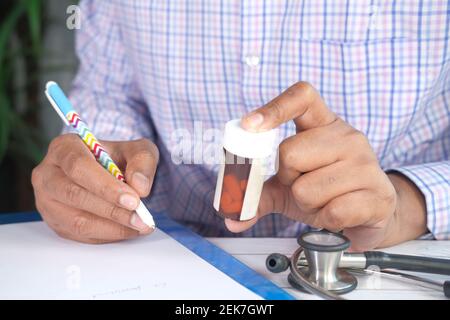 doctor hand writing prescription and holding a medicine container  Stock Photo