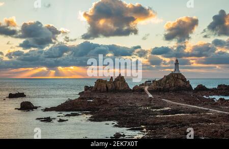 Road to La Corbiere lighthouse on the sea bottom in a low tide with cliff and sunset,  bailiwick of Jersey, Channel Islands Stock Photo