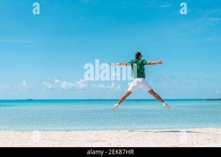 Happy young man jumping with outstretched arms on the beach. Summer vacation concept. Stock Photo