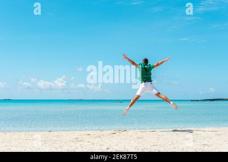 Happy young man jumping with outstretched arms on the beach. Summer vacation concept. Stock Photo