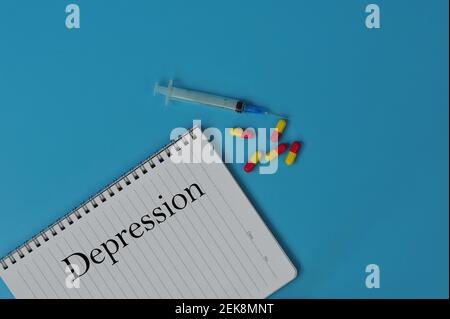Layout of Note book, pills and syringe with the text DEPRESSION on blue background Stock Photo