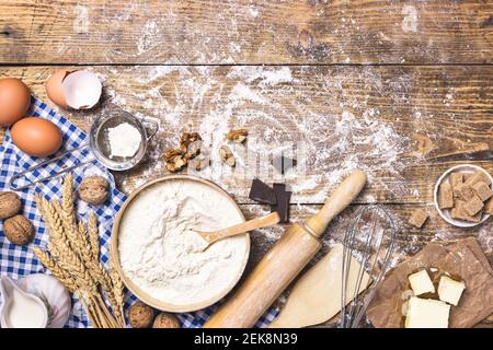 Frame of baking and cooking pastry or cake with ingredients and utensils. Eggs, nuts, sugar, butter, milk, flour and wheat on rustic wooden background Stock Photo