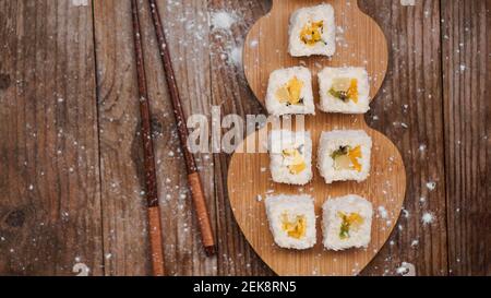 Sushi delivery. Sweet rolls made from rice, pineapple, kiwi and mango. Rolls on a wooden background. Wooden sticks for sushi. Stock Photo
