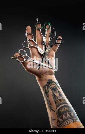 Hand of barber with equipment set on black table background. Close up different sccissors, razors, professional tools of hairdresser. Professional occupation, art, self-care concept. Magazine. Stock Photo