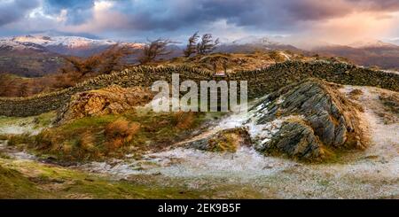 Rural stone wall and wooden stile with dramatic Winter panoramic view of snowcapped mountain range. Black Fell, Lake District, UK. Stock Photo