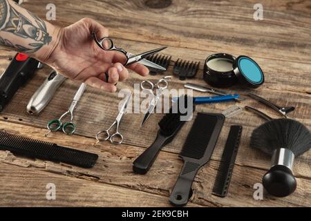 Hand of barber with equipment set on wooden table background. Close up sccissors, comb, brushes, razors, professional tools of hairdresser. Professional occupation, art, self-care concept. Magazine. Stock Photo