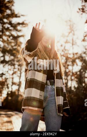 Young woman gesturing while standing at park during sunny day Stock Photo