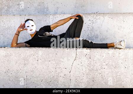 Man wearing white mask resting while lying on wall Stock Photo