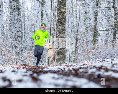 Young male athlete jogging with Labrador retriever during winter in forest Stock Photo