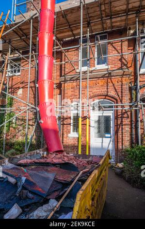 Rubbish chute for rubble, litter & building waste to be placed in a metallic skip on a construction site at a house covered in scaffolding in the UK. Stock Photo