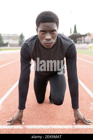 Confident sportsman in ready position to run on running track Stock Photo