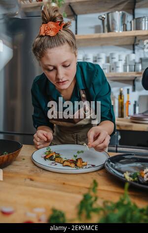 Young female chef garnishing dish while standing in kitchen Stock Photo