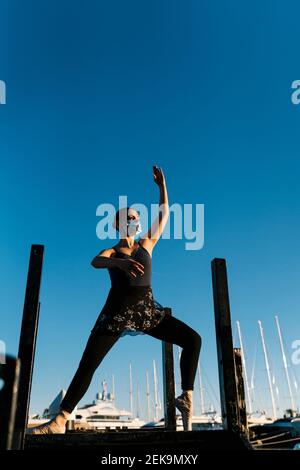 Young female ballet dancer practicing on jetty against blue sky Stock Photo