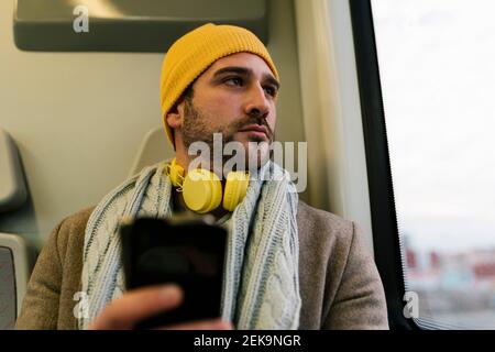 Mid adult man with mobile phone looking away while sitting in train Stock Photo