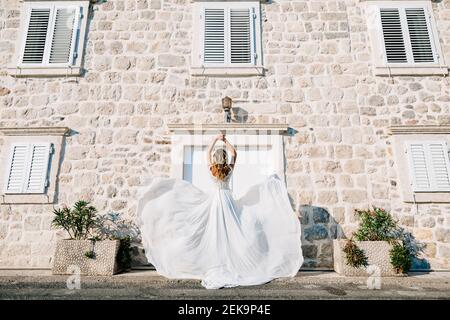 A bride in a wedding dress is spinning on the old street of Perast, her skirt flutters in the wind  Stock Photo