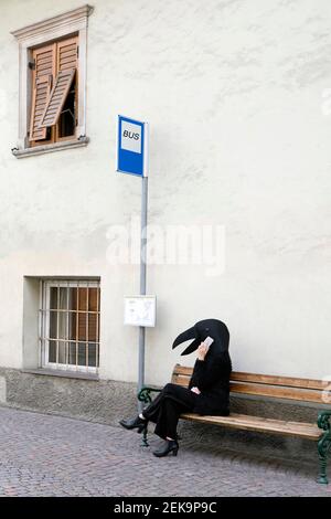 Female in crow costume talking on mobile phone while sitting at bus stop Stock Photo