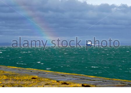 Edinburgh, Scotland, UK. 23rd Feb 2021. Kommandor Susan Offshore Tug/Supply Ship and rainbow in the Forth Estuary seen from Granton harbour breakwater on a blustery, sunny and rainy afternoon.  Credit: Craig Brown/Alamy Live News Stock Photo