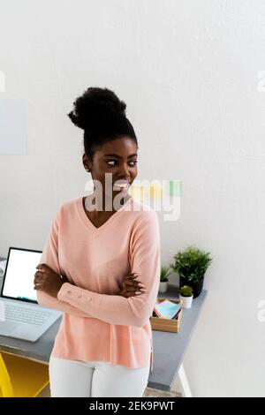 Female professional with arms crossed looking away while standing at home office Stock Photo
