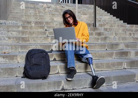 Smiling man with leg prosthesis using laptop while sitting on steps Stock Photo