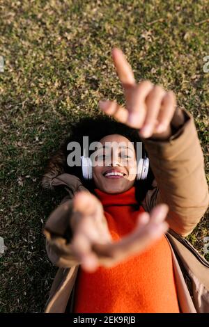 Smiling woman listening music and gesturing while lying on grass at park Stock Photo