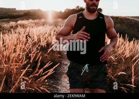 Male sportsperson running through dried grass field during sunset Stock Photo