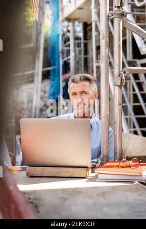 Smiling architect using laptop while sitting at construction site Stock Photo