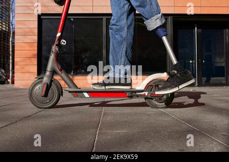 Young disabled man with prosthetic leg standing on electric push scooter Stock Photo