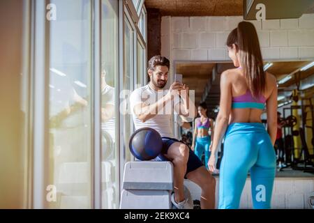 Picture of strong handsome man taking picture of his girlfriend in a bright gym. Stock Photo