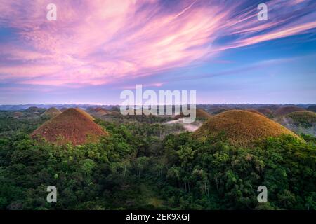 The famous Chocolate Hills of Bohol during sunset with whispy purple clouds and a cloudy fog drenched forest below Stock Photo