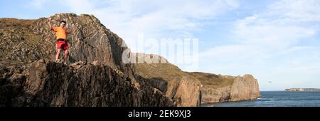 Cheerful mature male rock climber with arms raised standing on cliff Stock Photo