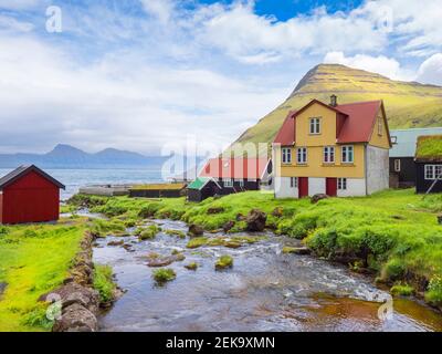Stream flowing by houses against cloudy sky, Iceland Stock Photo