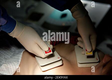 Hands of doctor holding defibrillator on patient's chest in hospital Stock Photo