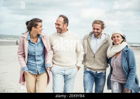 Group of adult friends walking side by side along sandy beach Stock Photo