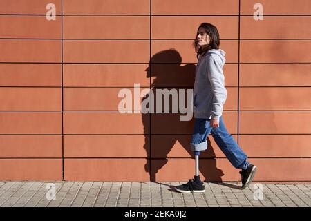 Disabled man with prosthetic leg walking by wall while looking away Stock Photo
