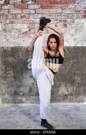 Mid adult female dancer practicing against old brick wall in factory Stock Photo