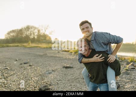 Smiling father giving piggyback ride to son against clear sky at evening Stock Photo