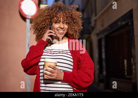 Smiling woman looking away while talking on mobile phone standing outdoors Stock Photo