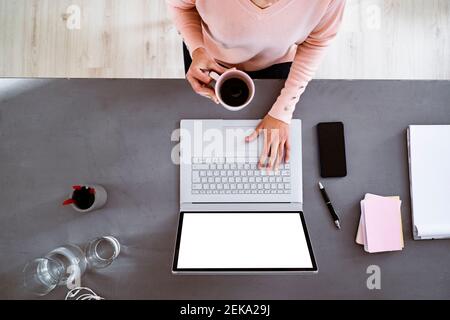 Young woman having coffee while using laptop while sitting at home Stock Photo