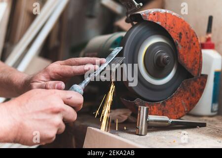 Male carpenter sharpening chisel using grinder in workshop Stock Photo