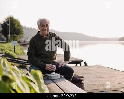 Smiling man drinking coffee while sitting on bench Stock Photo